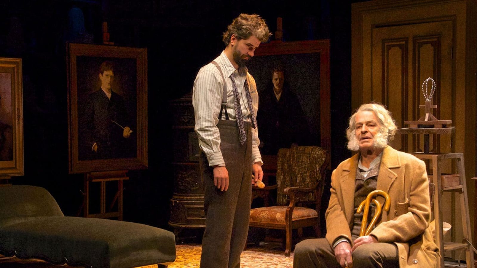 Two men in period clothing in an artist's studio, surrounded by portraits. One man holds a cane.