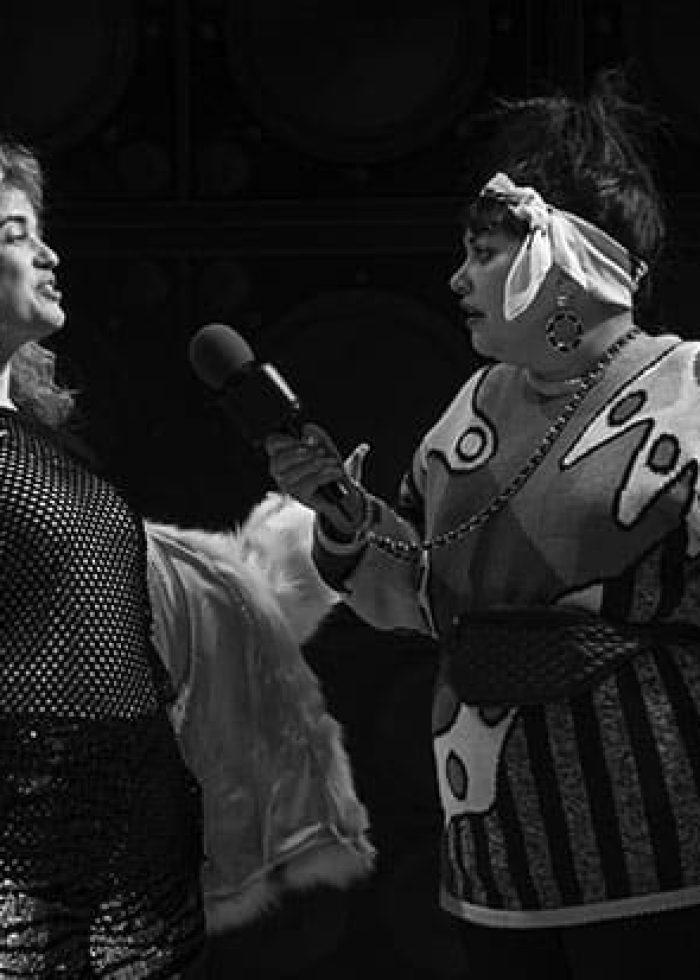 Two people on stage, one holding a microphone, in a black and white photo.