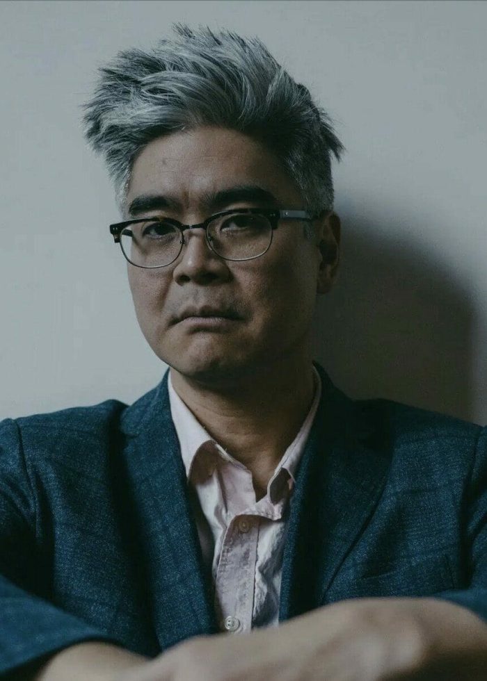 Lloyd Suh, playwright, wearing glasses and a blazer, looking directly at the camera.